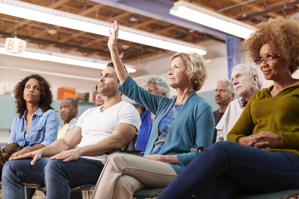 Older woman raises hand to ask a question at a community presentation