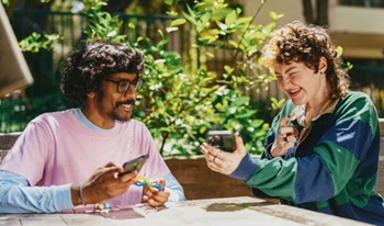 Two friends at a table discussing an electronic device