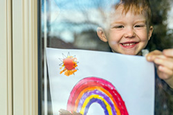 child behind window showing drawing of rainbow