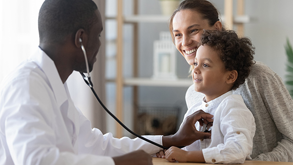 Doctor putting a stethoscope on the chest of a child sitting on the lap of his smiling mother