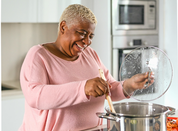 Woman cooking at the stove, stirring a pot with a lid in her other hand 