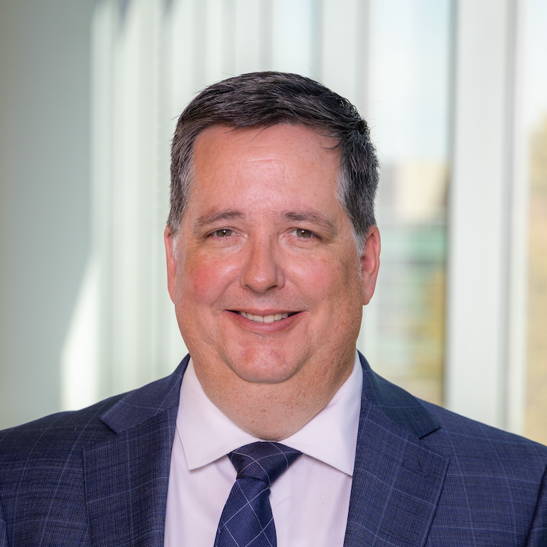 man in a blue suit and tie, smiling for a headshot