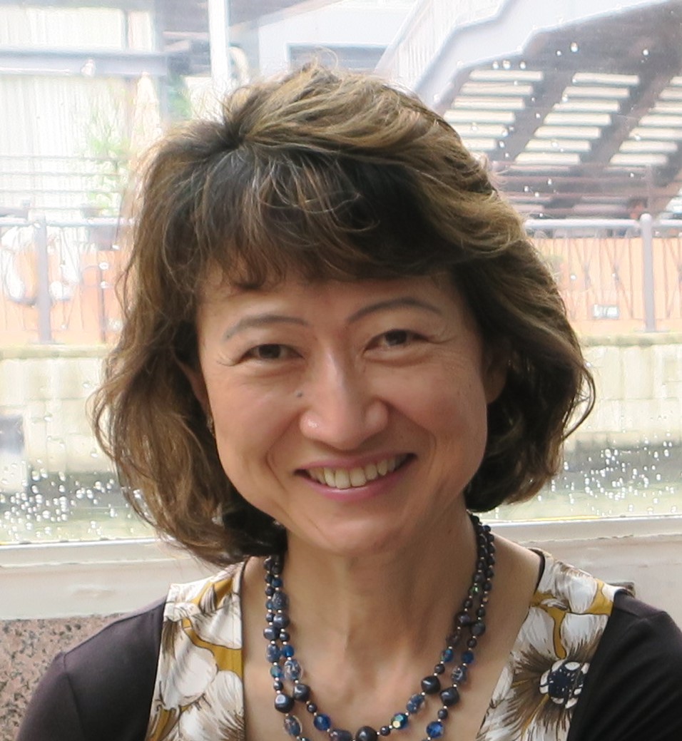 Mayumi Fujita smiling, wearing beaded necklaces and a flower shirt.