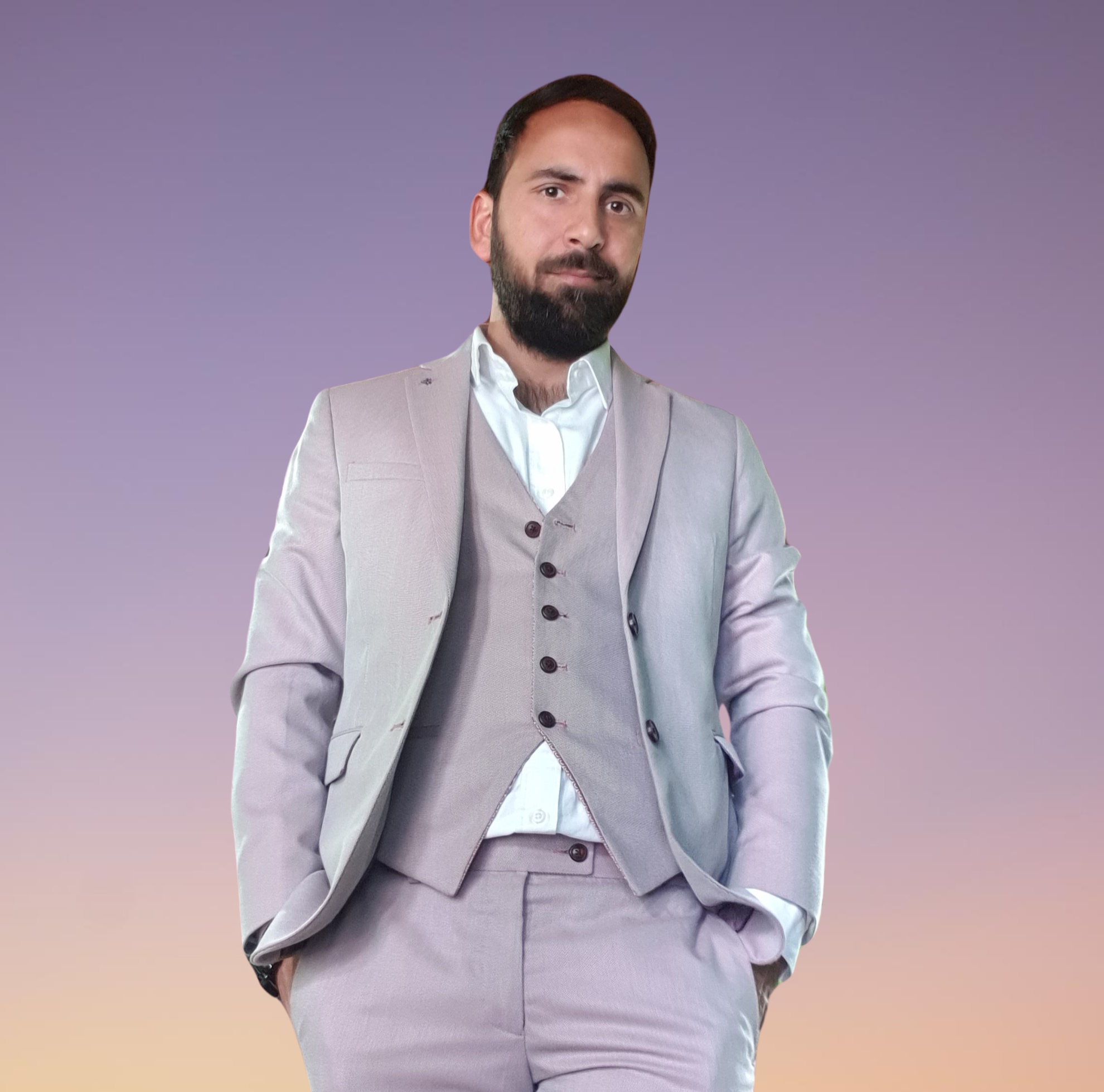 Shahid Naikoo standing with hands in pockets, wearing a three piece gray suit, against a purple and pink sunset sky.