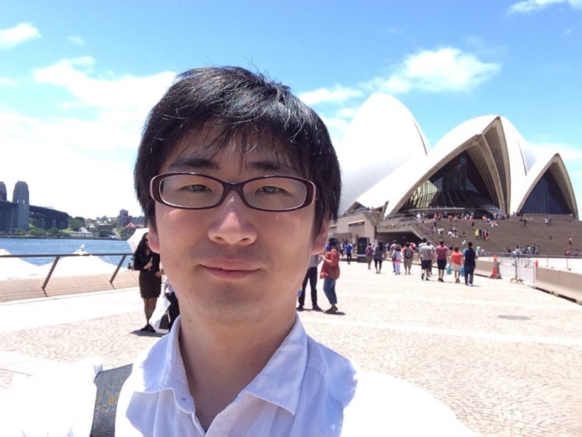 Takeshi Yamauchi smiling on a sunny day, standing in front of the Sydney Opera House.