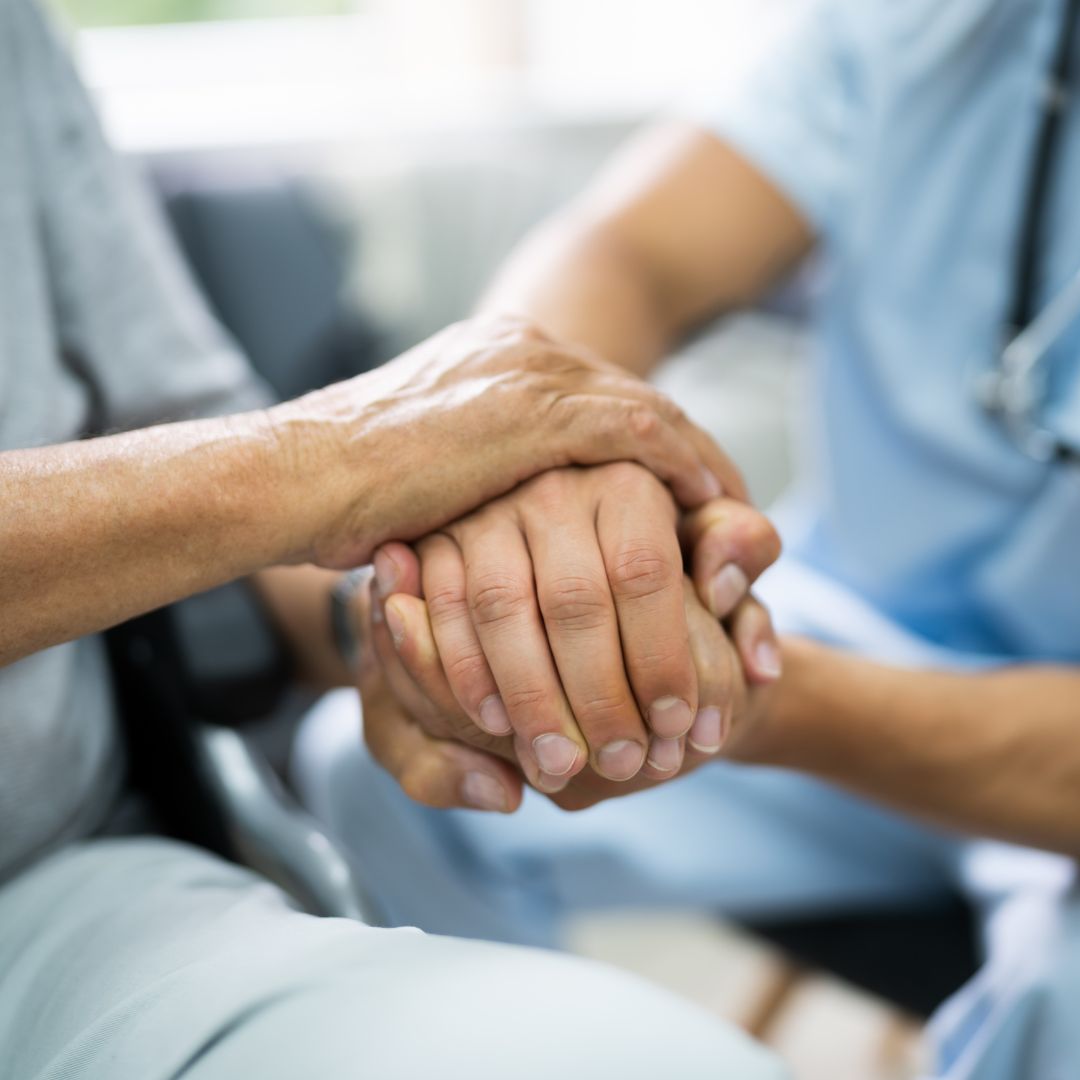 Older adult and nurse clasping hands.