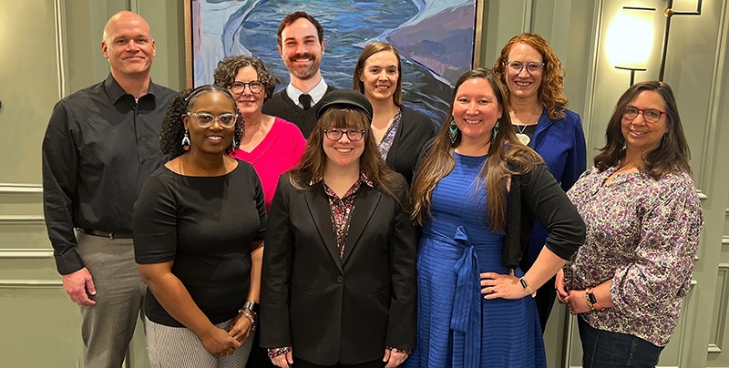 AEOgroupphoto9peoplestandinginfrontofawaterpainting