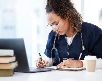 Student in scrubs writing in a book while studing