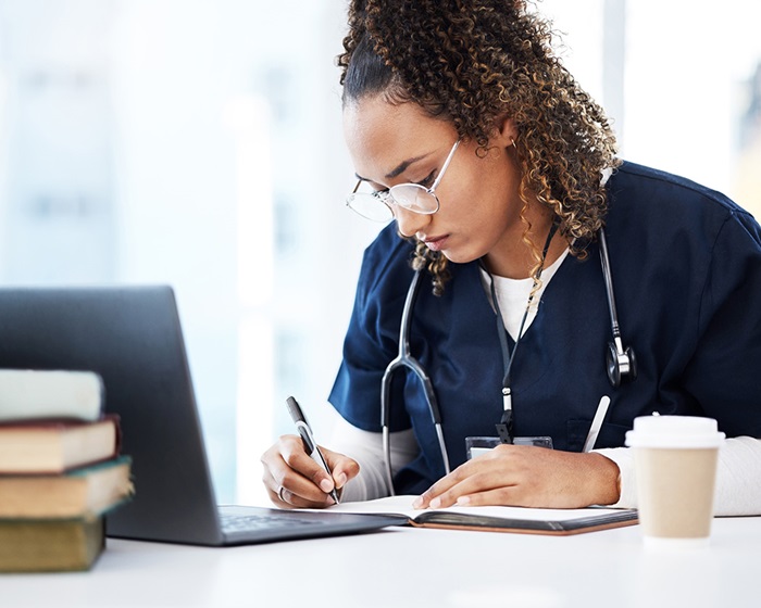 Studentinscrubswritinginabookwhilestuding