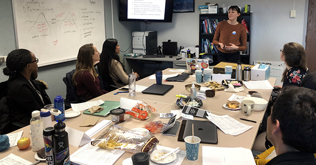 Maggie Kriz (Kuusinen) leading a seminar discussion in a small conference room. 