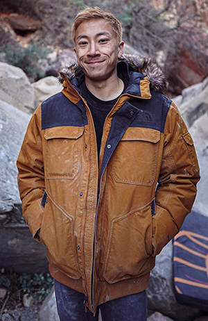 Tristan Chen standing in front of boulders wearing a brown jacket.