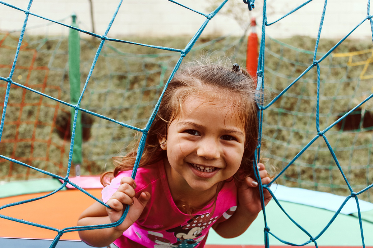 smiling child peering through net on a trampoline