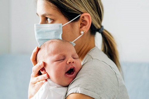 womaninfacemaskholdinginfant