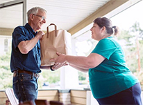 woman handing bag of food to elderly man