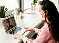 womanwearingfacemasklookingatcomputerwhereanotherwomaniswearingafacemask