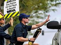 twofirefighterswithsignandbootsolicitingfundsfrompassingcar