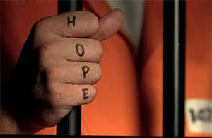 Inmate's hand behind bars, with tattoo reading HOPE
