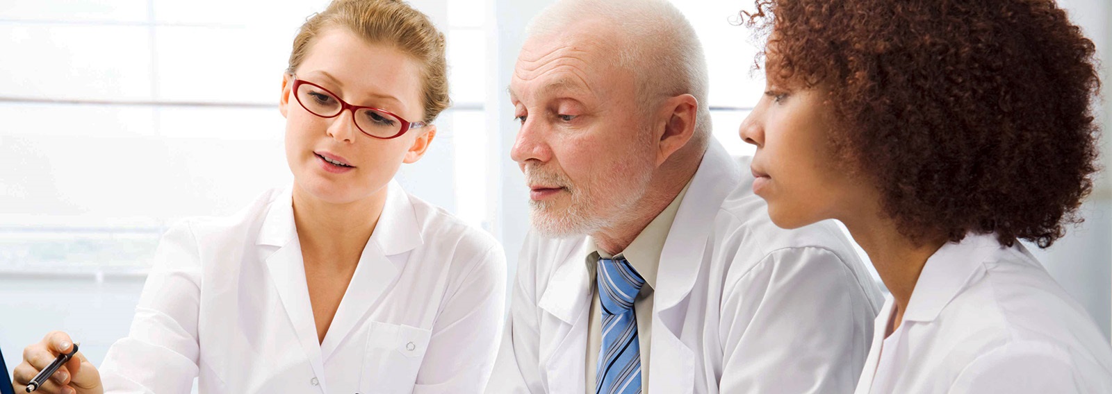 threemedicalprofessionalsatalaptopwearingwhitecoatsWhitewindowinbackground