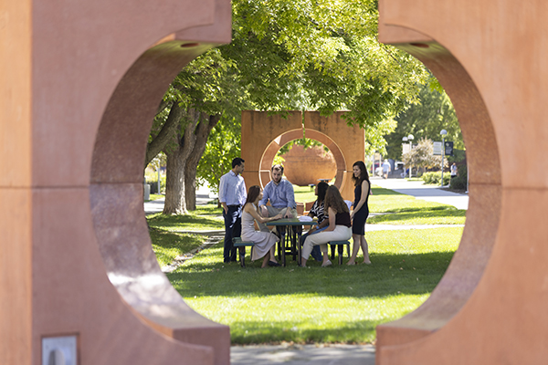 Students, viewed through sculpture, talking at picnic table