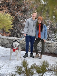 Nick F. and Lizzy G.  with dog standing in front of low stone wall.