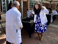 Matriculantonstagewearingwhitecoatandstethoscopewalkingtowardfacultymember