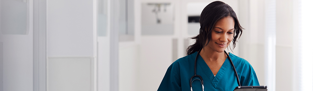 Woman in scrubs looking at clipboard in hospital hallway