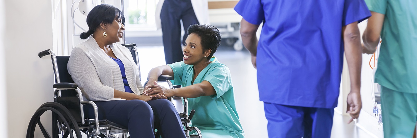 Studentsquattingtalkingtowomaninwheelchairinmedicalsetting