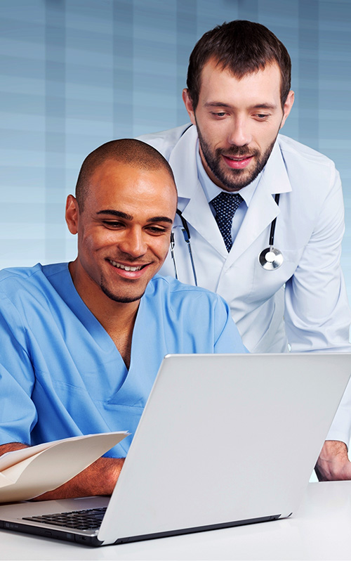 student in scrubs on laptop with doctor standing looking at screen