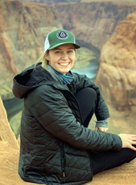 Helena Heister wearing black puffy coat, sitting on ledge over canyon.
