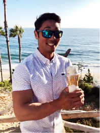 Kevin Paik standing at a beach, holding an ice cream cone. Dressed in white.