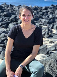 Michelle Wehbe sitting on a rocky beach. Wearing jeans and black top.