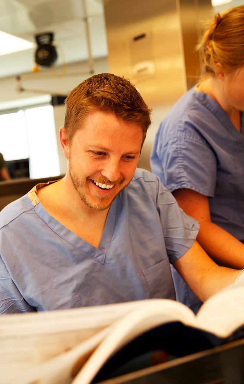 Studentwearingscrubslaughingandpagingthroughalargebook