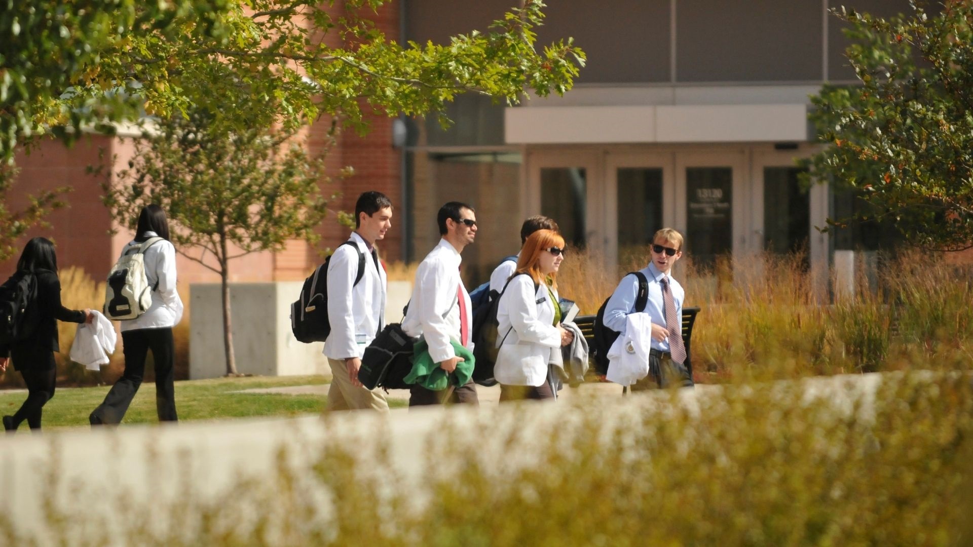 Groupofdoctorswalkingthroughcampusinwhitecoatssuitsandsunglasses