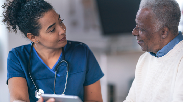Blacknursewearingblueconsultswithpatientinwhitesweater