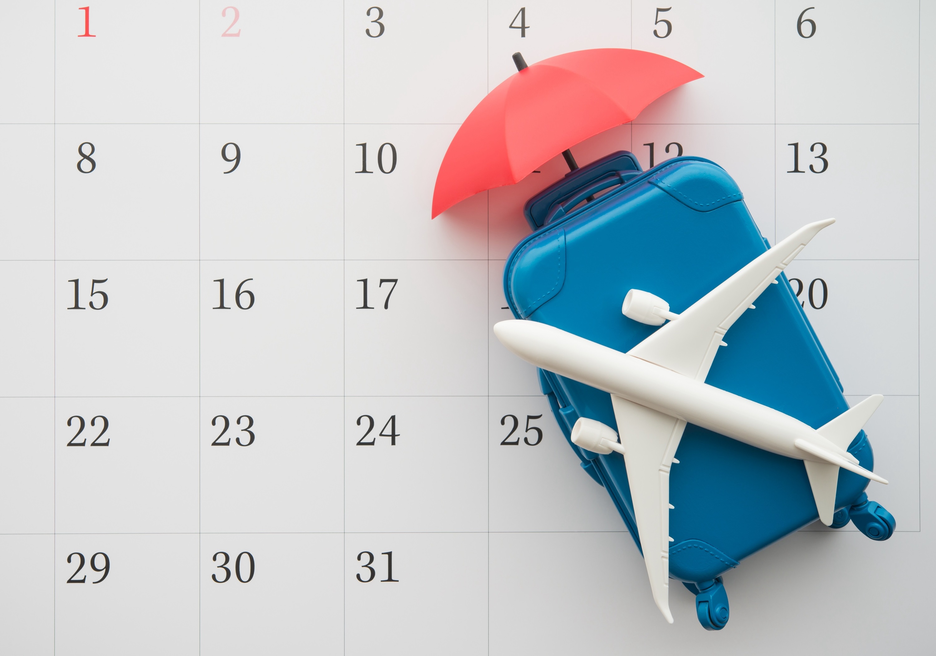 Photoofasmalltoyairplaneandumbrellaontopofasuitcaseagainstacalendarbackdrop