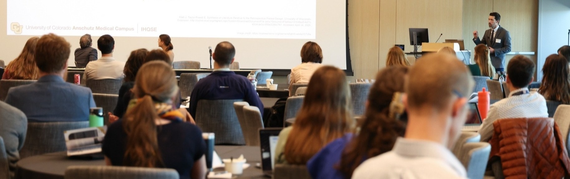 Speakerpresentinginfrontofalargeaudiencewithslidesprojectedonalargescreen