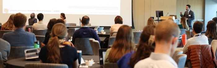 Speakerpresentinginfrontofalargeaudiencewithslidesprojectedonalargescreen