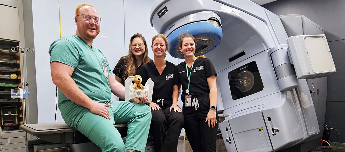 TristanSeawaltposeswithradiationoncologyresidentsfellowsatCSUsFlintAnimalCancerCenterataLINACradiation-therapymachineusedtotreatveterinarypatients