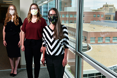 Three faculty wearing masks standing in hospital by window