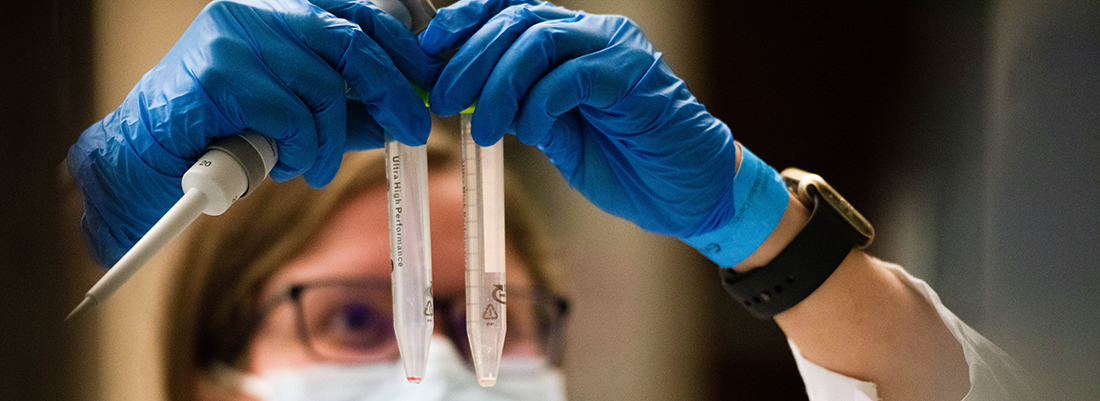 researcherwearingmasklookingupwardattwovialsshesholding