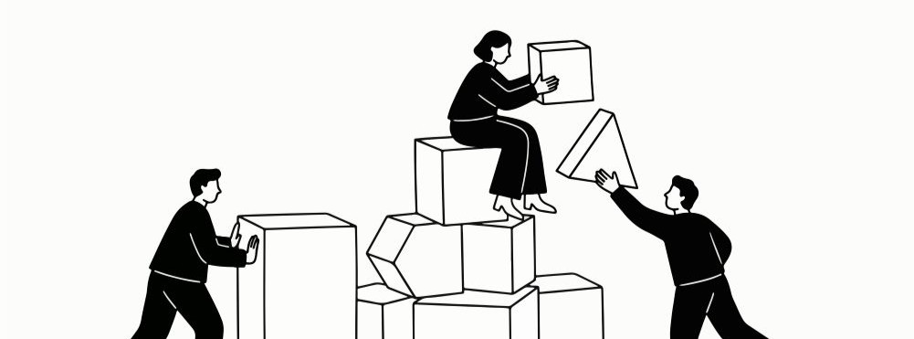 Three people work together stacking different shaped blocks; one person sits on top, another passes a triangular block, and the third pushes a rectangular block.