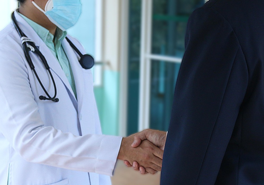 A person in a pink sweater holds a gray inhaler in one hand and a red cap in the other, showing asthma medication preparation.