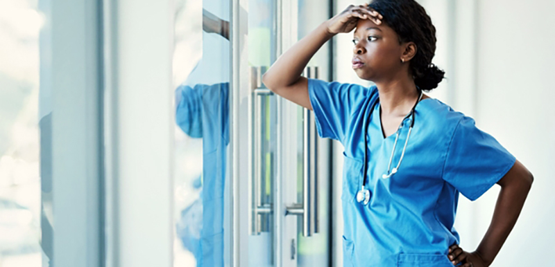 health care worker with and to brow leaning against window