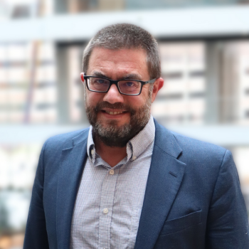 Headshot of a man in a blue suit with glasses on