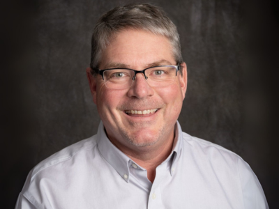 Man smiling in glasses and grey button up shirt
