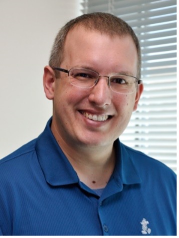 Headshot of a man with glasses in a blue polo shirt