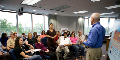 older man in blue shirt presents to a room of various people
