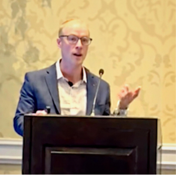 Bald man in glasses presenting at a podium