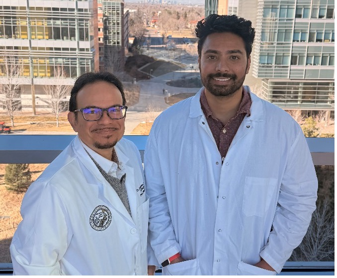 Two men standing side by side, one in glasses