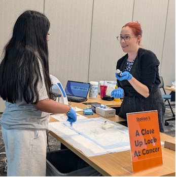 Girl with long hair talks to redhead woman across a table with pamphlets